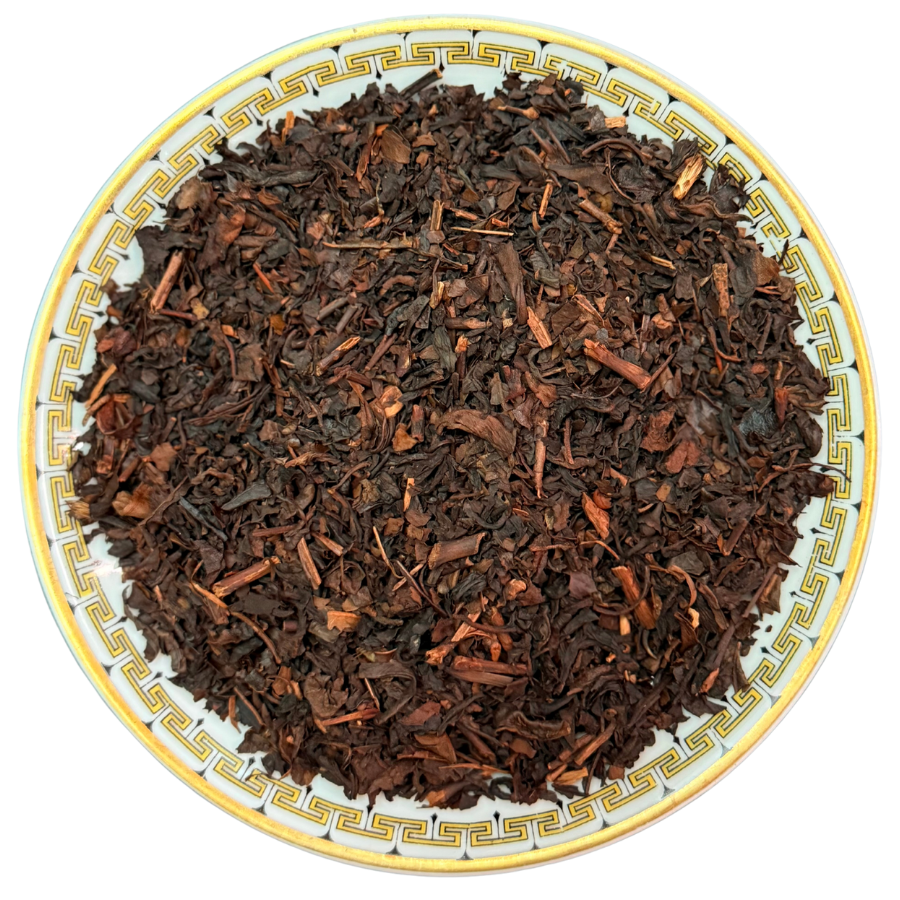 Dry black tea leaves on a decorative plate with a white background