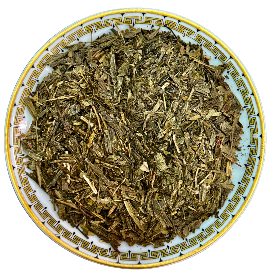 Dry green tea leaves on a decorative ceramic plate with a white background