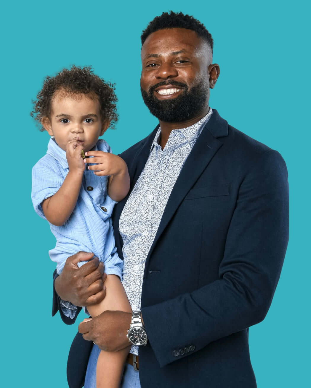 Co-Founder Guerby Joseph in a suit holding his son Denzel