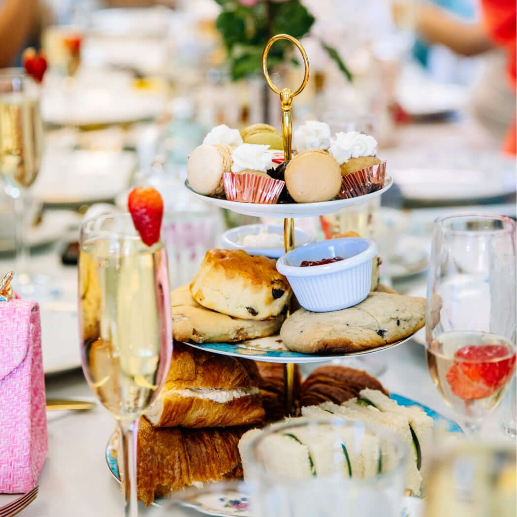 Three-tiered cake stand with pastries and a glass of champagne on a table.