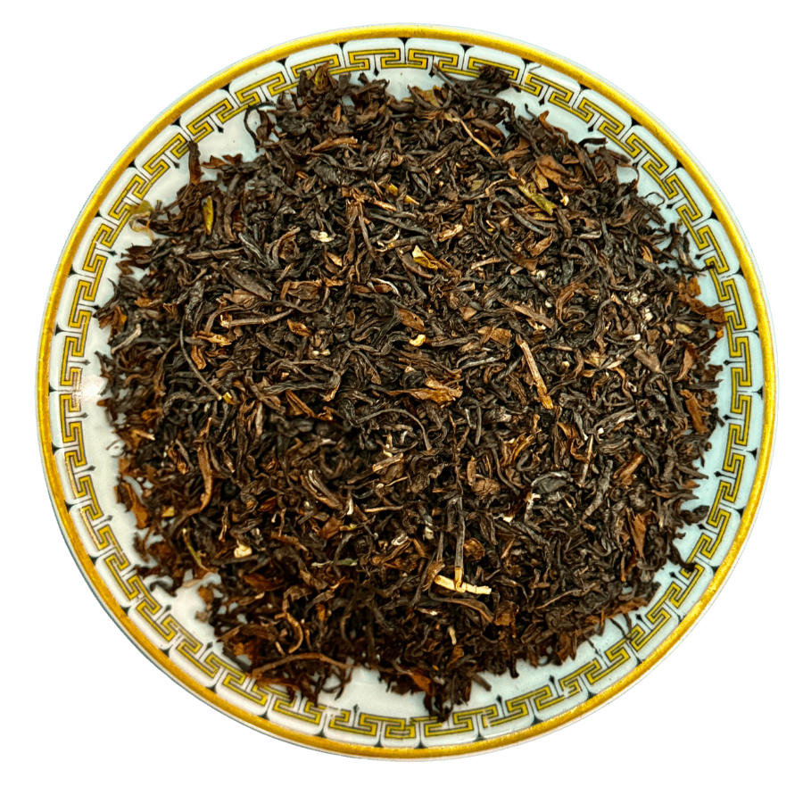 Dry black tea leaves on a decorative ceramic plate with a white background