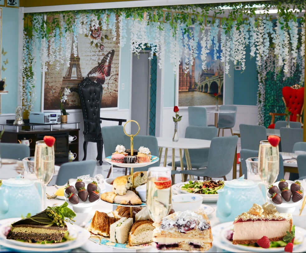 Dessert table with various pastries and drinks in a decorated room with wall art and furniture.